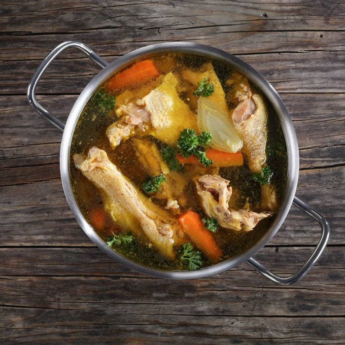 clear Chicken broth with pieces of rooster meat on bone and vegetables in a metal casserole on dark wooden table, view from above; Shutterstock ID 776860549
