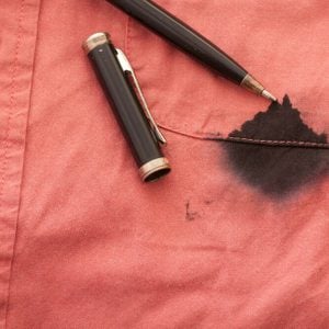 A Close Up of a Broken Pen Resting on the Men's Red Shirt Stained with Ink