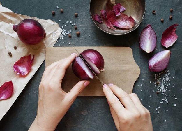 Person slicing red onions on a cutting board