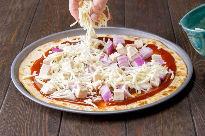 Sprinkling Cheese Over Onions and Chicken on Pizza Crust, Wooden Background