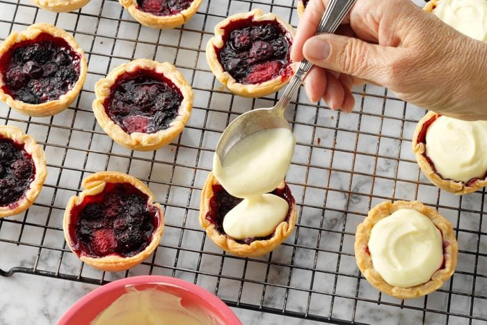 A Hand Holding a Spoon Over a Small Fruit Tarts