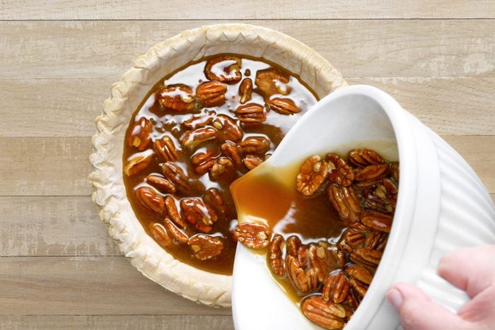 Pecans are being poured in a pie crust