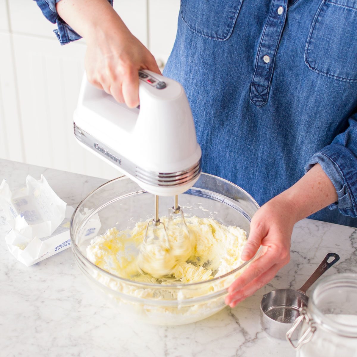 Mixing Butter, Sugar, Salt, Egg, Vanilla Extract and Almond Extract In a Large Glass Bowl with Hand Mixer on Marble Kitchen Top