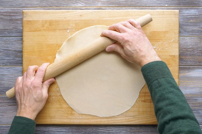 Rolling Out Dough on a Wooden Board with a Rolling Pin