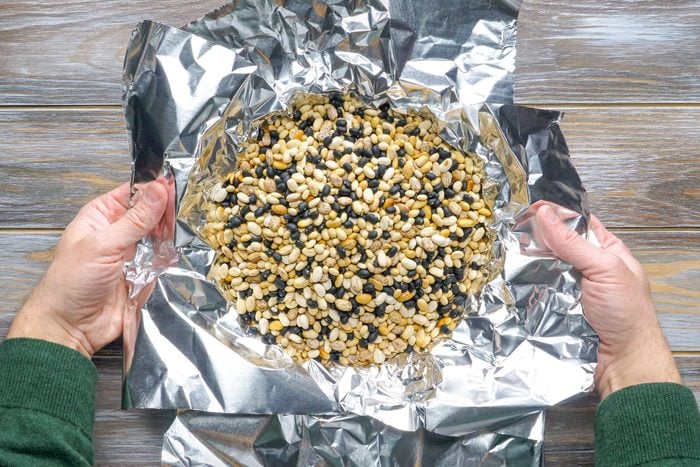 Dried Beans in Aluminium Foil in Someone's Hands on Wooden Surface
