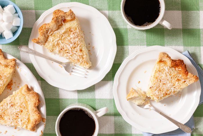 Coconut Custard Pie in Ceramic Plate with Coffee in Cups and Sugar Cubes in Small Bowl with Forks on Plate
