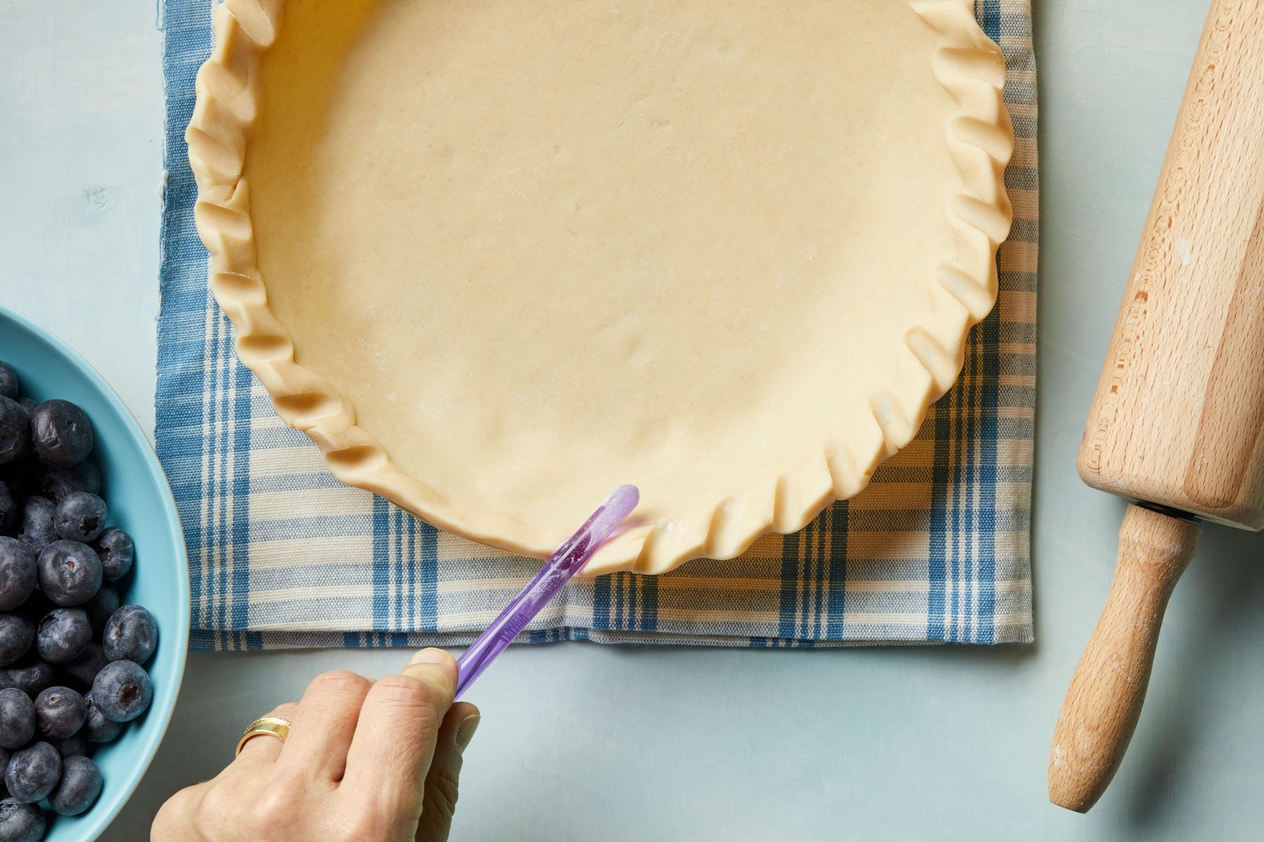 A hand holding a purple tweezers over a pie crust