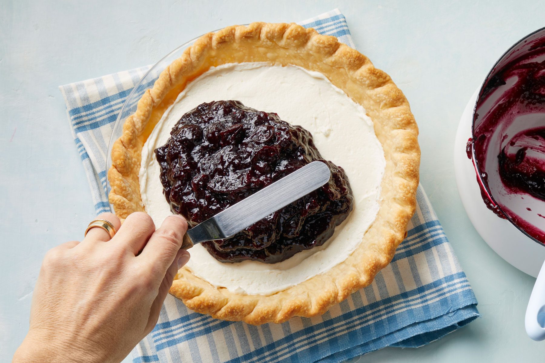 A person spreading cream cheese and blueberry paste on a pie