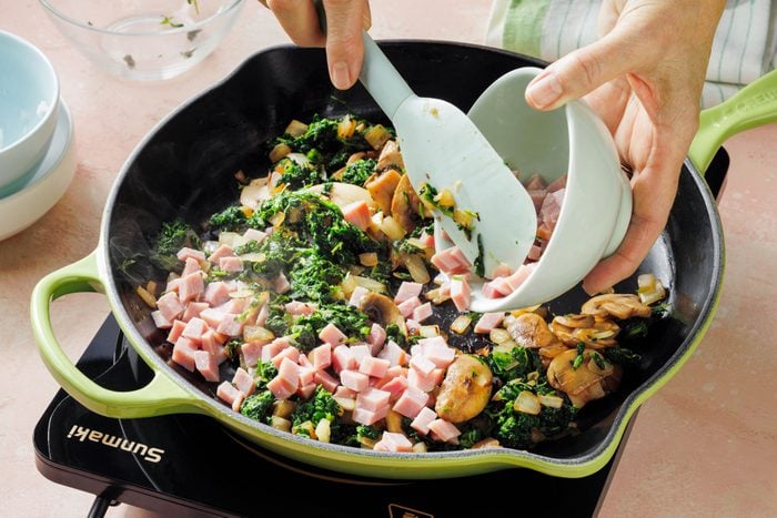 Sautéing spinach, ham, onions and mushrooms in a large skillet on an induction cooktop.