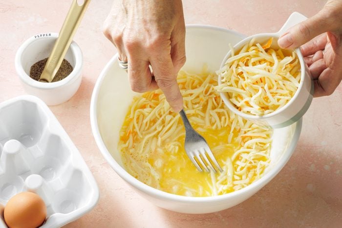 adding cheese into a bowl half filled with beaten egg