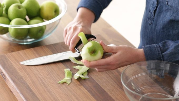 Person peeling a green apple