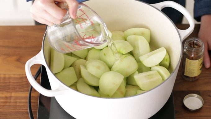 Person pouring water over peeled apples in a dutch oven