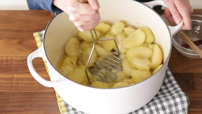 Person mashing cooked apples in a dutch oven