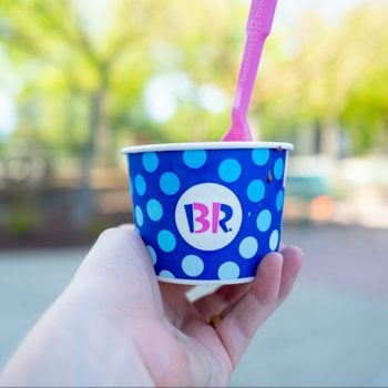 hand holding out a cup of baskin robbins ice cream outdoors on a sunny day