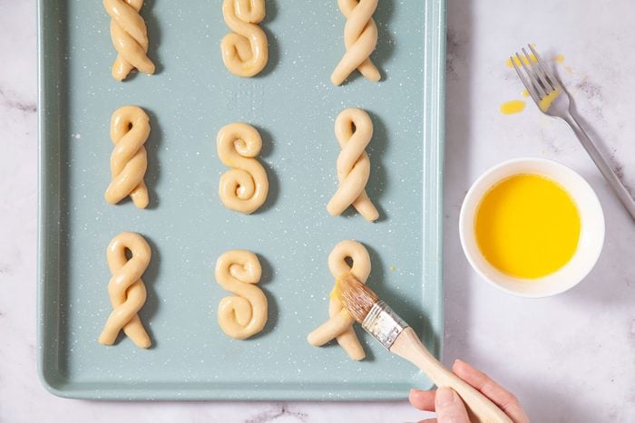 A person is preparing a tray of cookies with letters on it.