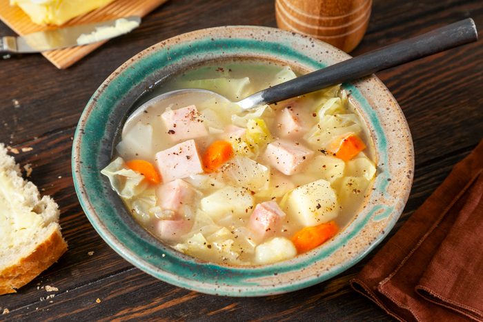 Ham And Cabbage Soup Served in Old-Fashioned Ceramic Bowl with Spoon on Wooden Surface