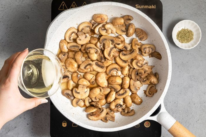 Pouring Wine into Mushrooms Sautéing in A White Non Stick Skillet on Induction Cooktop