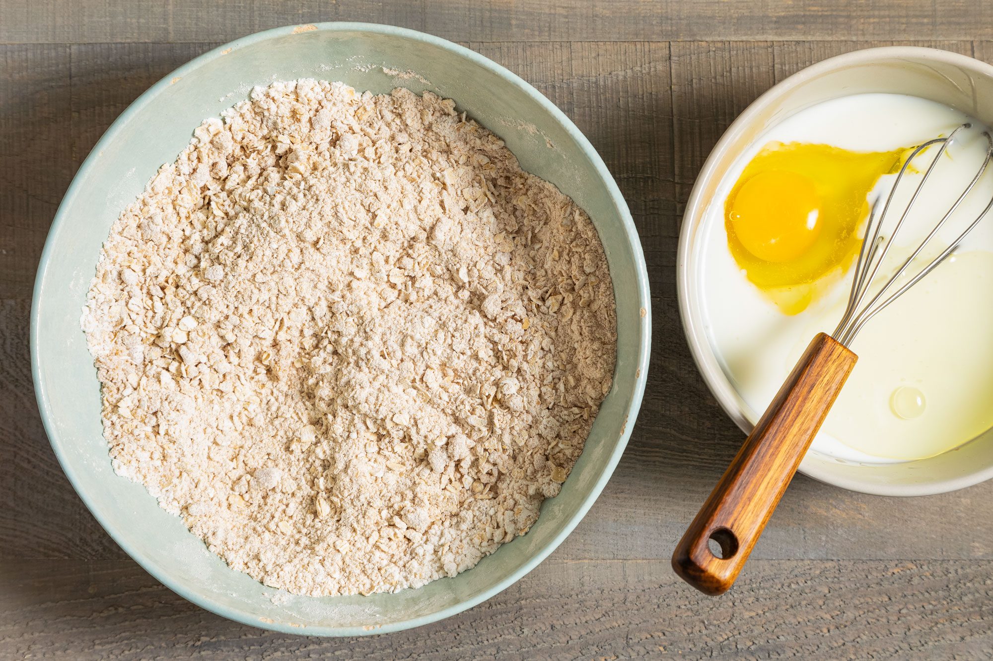 Oatmeal, Whole Wheat Flour Mix in Large Ceramic Bowl and Egg and Buttermilk in Another Bowl on Wooden Surface