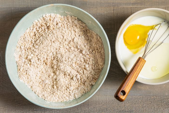 Oatmeal, Whole Wheat Flour Mix in Large Ceramic Bowl and Egg and Buttermilk in Another Bowl on Wooden Surface