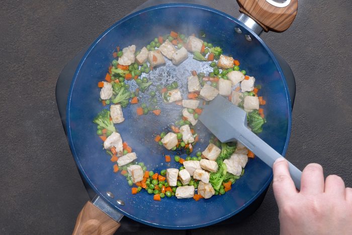 A person is frying vegetables in a wok.