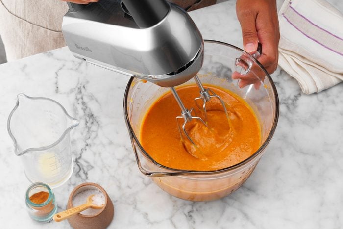 A Hand Holding a Mixer to a Bowl of Orange Liquid