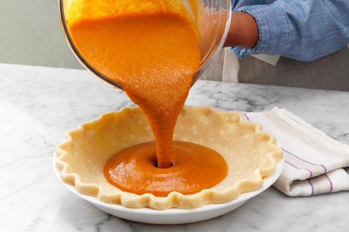 A Person Pouring Orange Liquid Into a Pie Crust