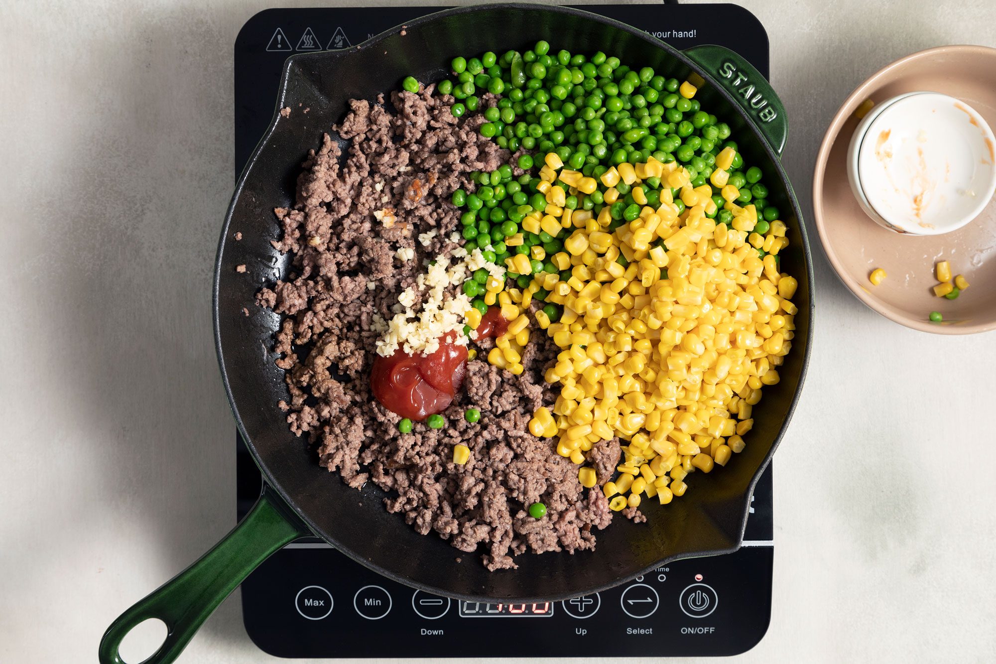 cooked beef, corn, peas, ketchup and garlic in a large skillet on induction cooktop
