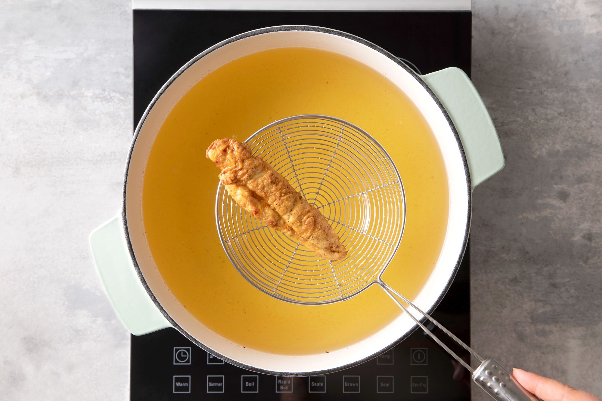 Frying Chicken Tenders in Hot Boiling Oil in a Pan on Induction Cooktop