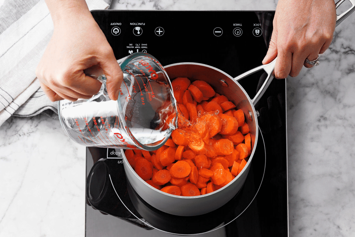 A Person Pouring Water into a Pot and Boiling the Carrots