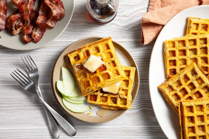 Sweet Potato Waffles topped with Butter and sliced apples and bacon on the side 