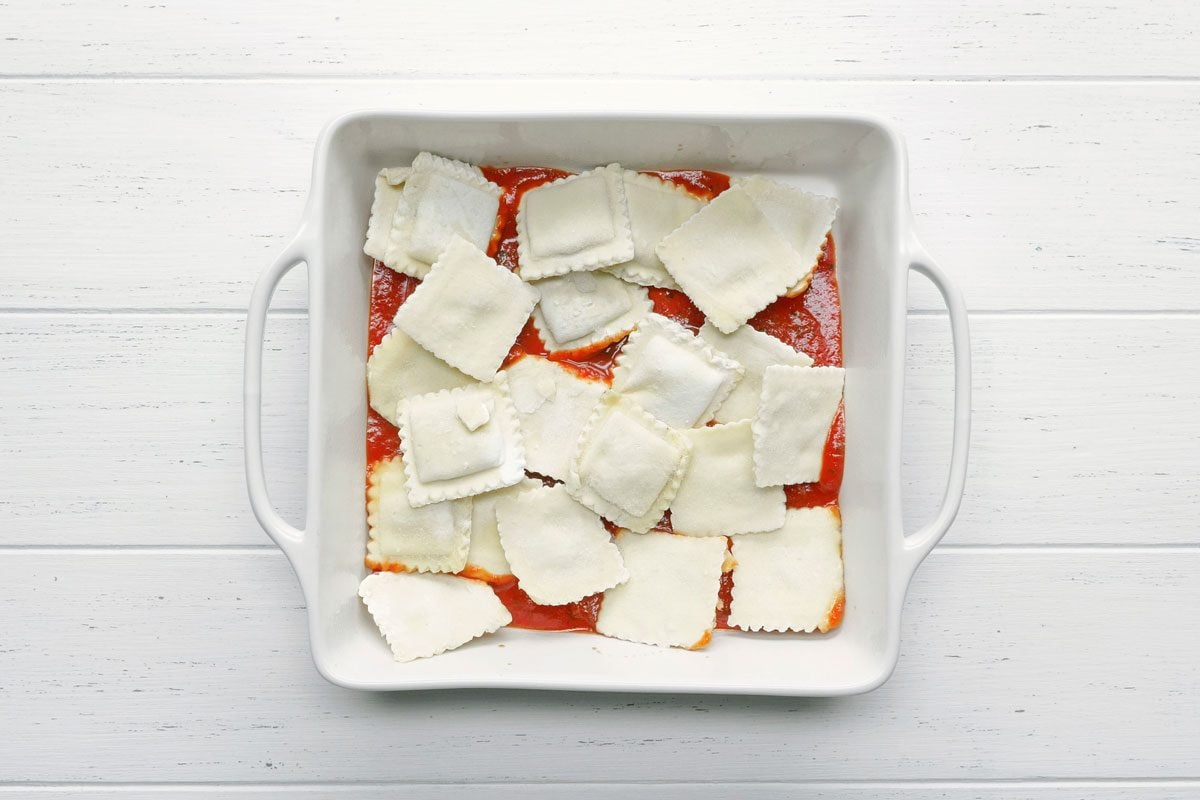 first layer of sauce and frozen ravioli in a square baking dish