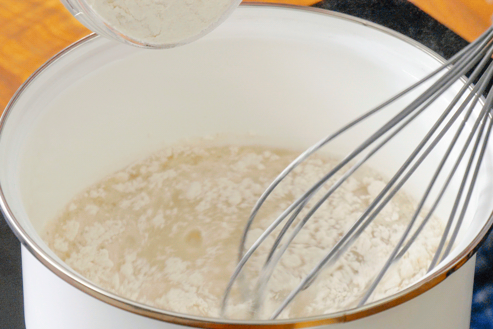 A whisk is being used to mix flour in a bowl.
