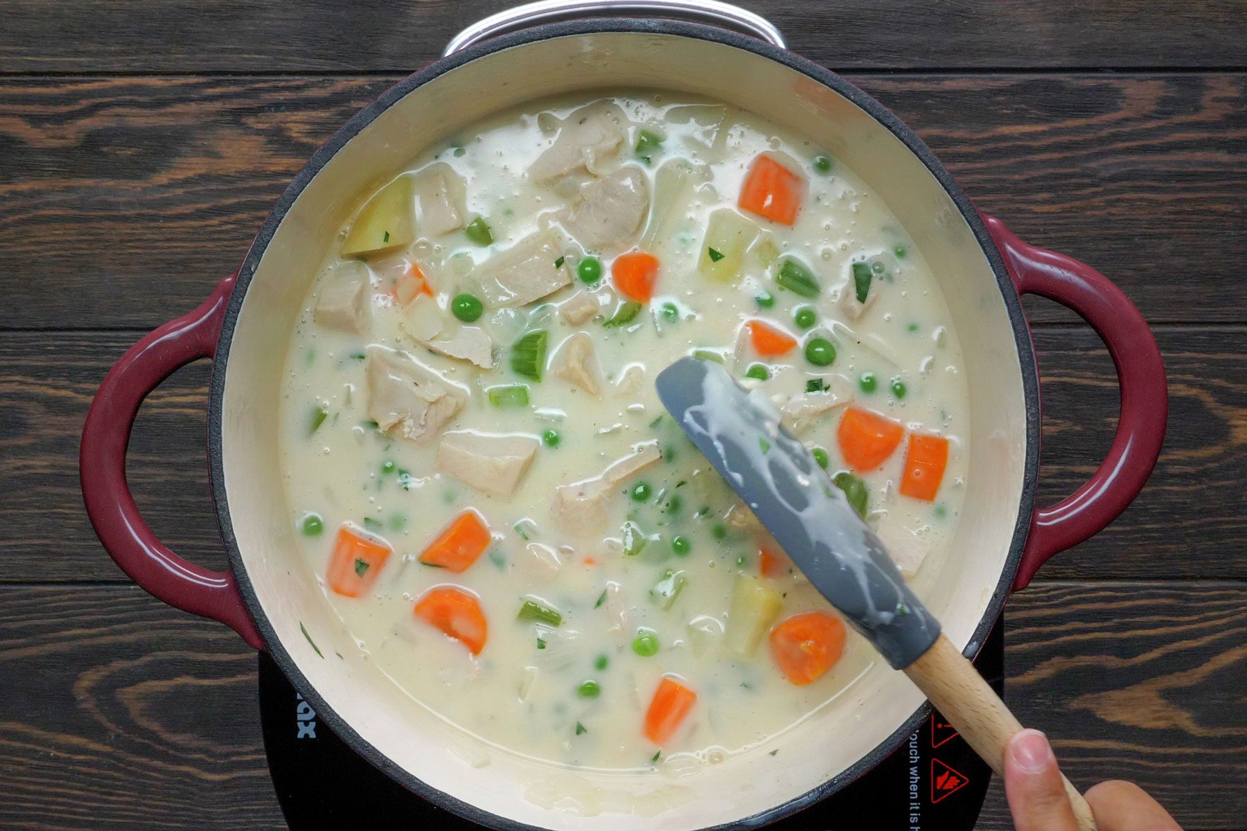Turkey cubes, frozen peas, cream is added in a pot with vegetables to make Turkey Potpies