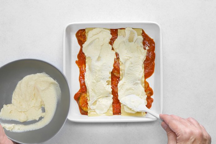 A person is preparing a lasagna in a pan