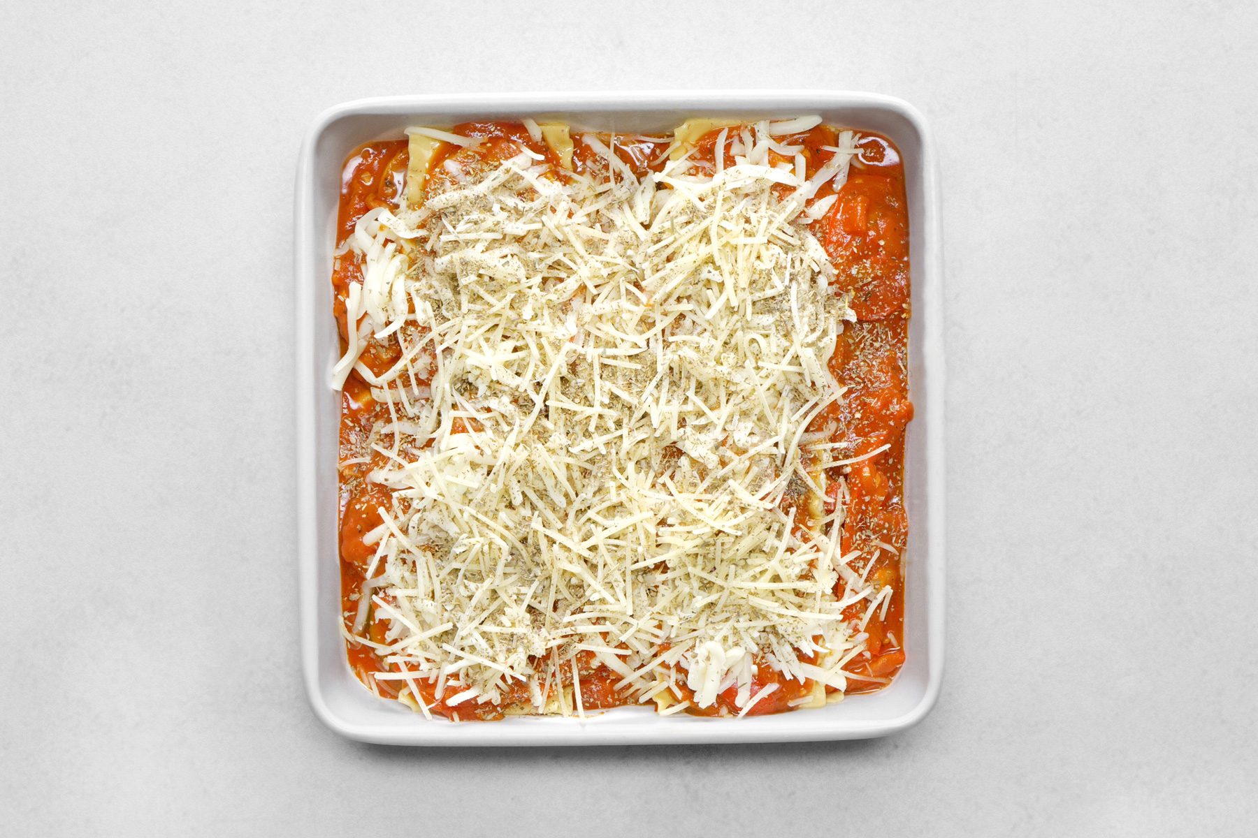 A white baking dish with cheese and sauce on it
