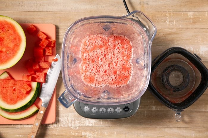 A blender with watermelon slices on a cutting board.