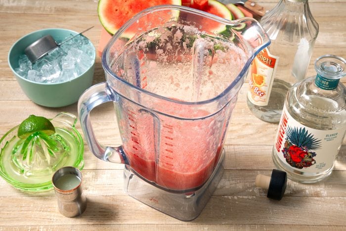Watermelon Puree in the blender and tequila, Triple Sec and lime juice on the side on a wooden table