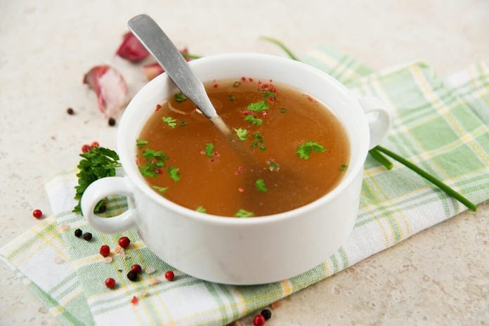 Bone Broth in Small Soup Bowl Served with Fresh Herbs, Garlic and Spices