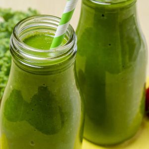 Close up of healthy green juice smoothie in glass bottle sitting on yellow napkin with fresh strawberries and kale