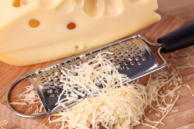 Grated cheese and grater on a wooden cutting board.