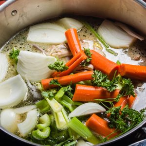A large stock pot on a stove with vegetables cut for making soup