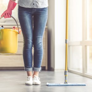 Cropped image of beautiful woman in protective gloves holding a flat wet-mop and bucket with detergents and rags while cleaning her house