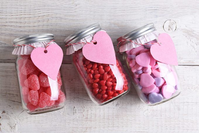 Canning jars laying on their sides filled with candy hearts and for Valentine's Day on a rustic wood table. The jars have blank heart shaped gift tags hanging from the neck