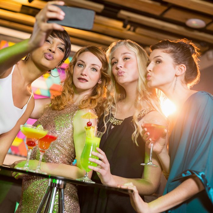 Group of friends taking selfie from mobile phone while having cocktail in bar; Shutterstock ID 585227993