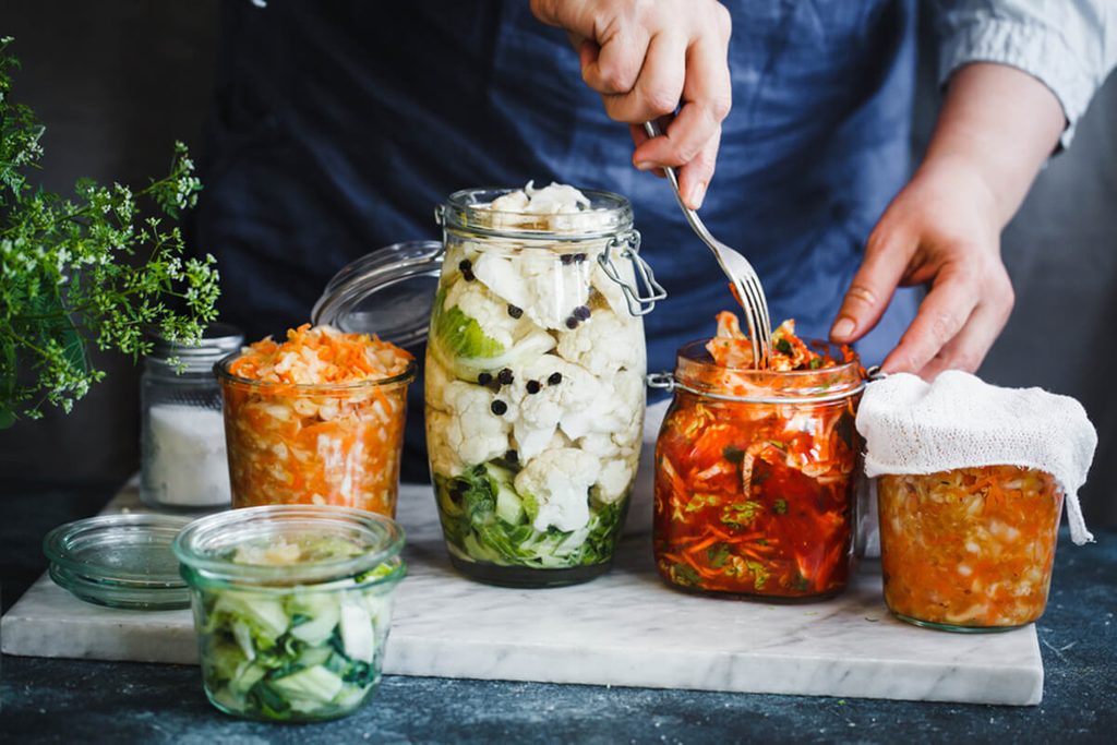 Cabbage kimchi, broccoli marinated, sauerkraut sour glass jars over rustic kitchen table.