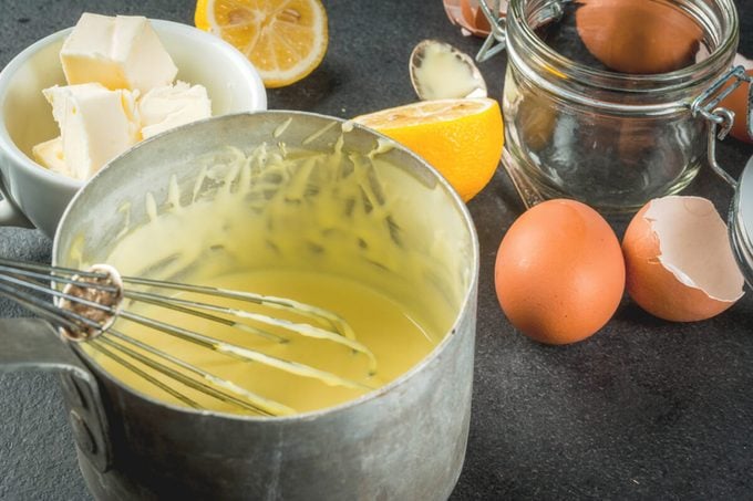 Hollandaise sauce in a metal saucepan, with ingredients for cooking - eggs, butter, lemons. 