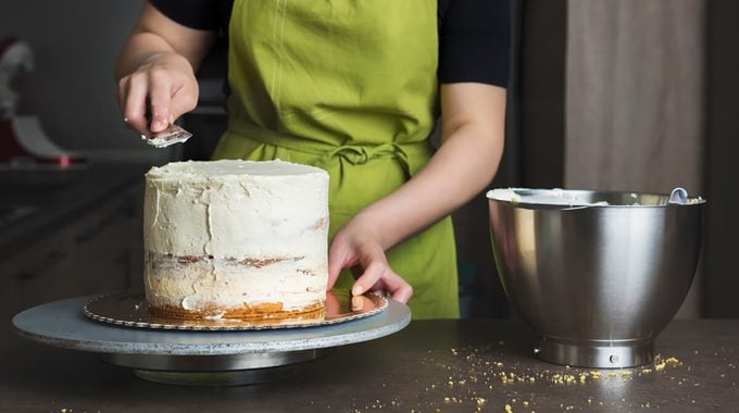 Unrecognisable woman decorating a delicious layered sponge cake with icing cream. DIY, sequence, step by step, part of series.