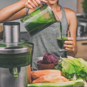 Woman juicing making green juice with juice machine in home kitchen. Healthy detox vegan diet with vegetable cold pressed extractor to extract nutrients for smoothie drink
