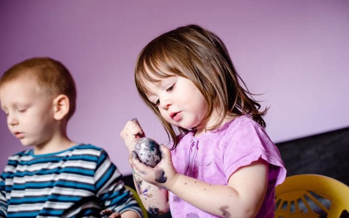 Close up of cute little girl using water colors, painting Easter egg, and her hands also