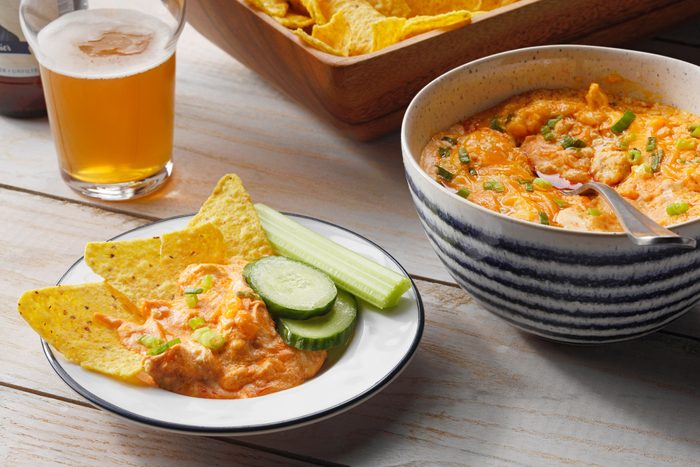 Slow Cooker Buffalo Chicken Dip in a bowl and served onto a plate with tortilla chips; beer nearby
